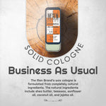 Business As Usual Solid Cologne in a slim vintage slide tin with a dark label, orange accents, and pale green base.
