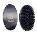 Essential Beard Comb Set includes a black oval beard brush with dense dark bristles and a gold-toned logo on the back.