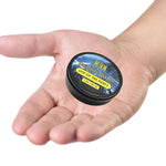 Life of the Party Beard Balm in a small black round tin with a blue and yellow label, held in an open hand.