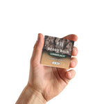 Lumberjack Beard Balm in a small square tin with a dark forest-patterned label and earthy brown tones.