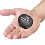 Unscented Beard Balm in a small black round tin with a screw-top lid and white label lettering, resting in a palm.